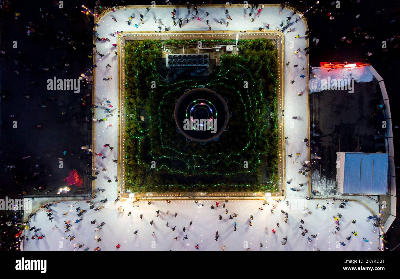 Bellissimo paesaggio urbano. Molte persone pattinano su una pista di pattinaggio all'aperto con illuminazione e ghirlande la sera d'inverno nel parco pubblico della città. Drone aereo Visualizza sfondo. Luci di Natale di Capodanno Foto Stock