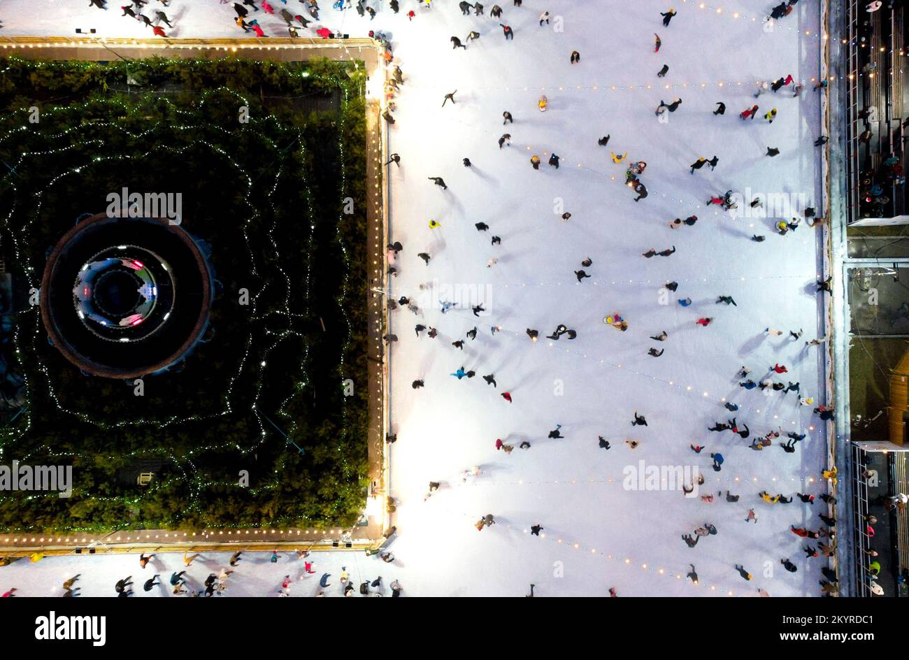 Bellissimo paesaggio urbano. Molte persone pattinano su una pista di pattinaggio all'aperto con illuminazione e ghirlande la sera d'inverno nel parco pubblico della città. Drone aereo Visualizza sfondo. Luci di Natale di Capodanno Foto Stock