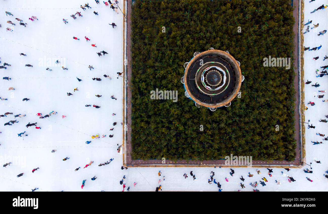 Aereo Drone View volo sopra molte persone in abiti colorati pattinare su pista di ghiaccio all'aperto in inverno. Vista dall'alto sul pattinaggio su ghiaccio urbano. City Park, pista di pattinaggio su ghiaccio Publik. Inverno all'aperto. Pattinaggio sfondo sportivo Foto Stock