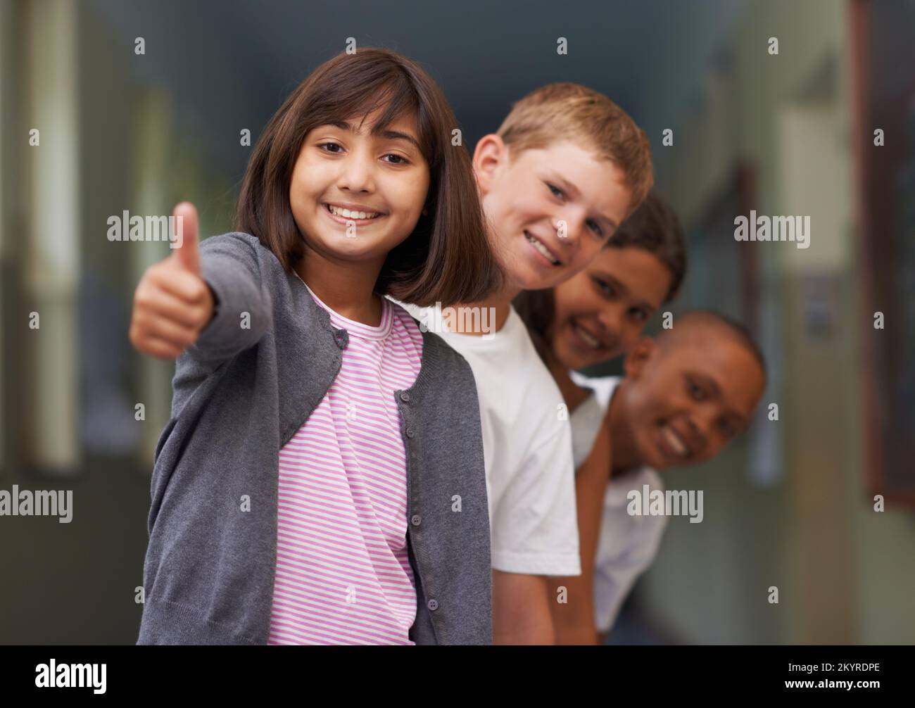 Sentirsi positivi per la scuola. Ritratto di una giovane ragazza che ti dà i pollici-up con i suoi amici dietro di lei. Foto Stock