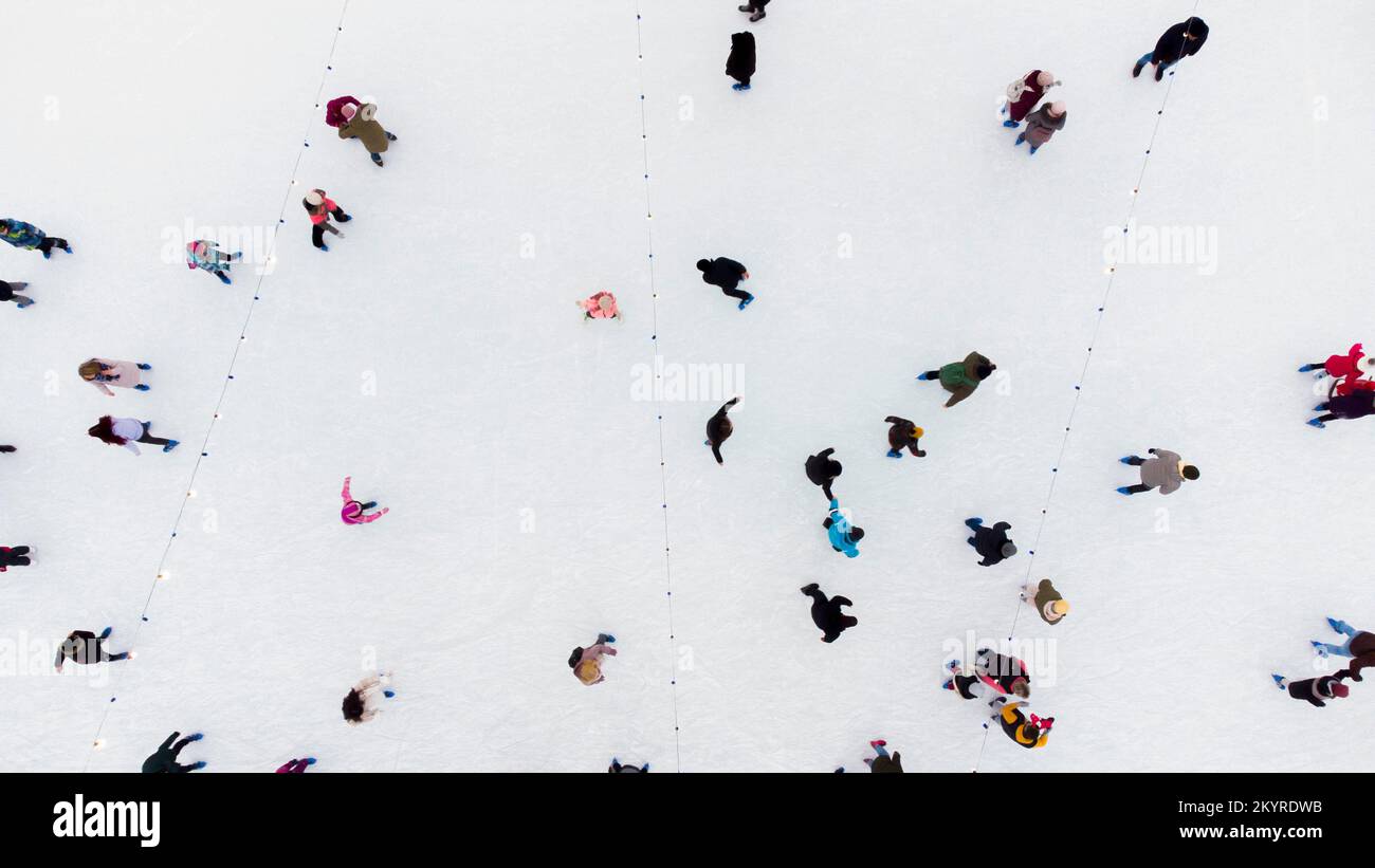 Vista dall'alto delle persone che pattinano sulla grande pista di pattinaggio all'aperto il giorno d'inverno. Aereo Drone Vista volo sopra folla di persone che pattinano su ghiaccio in pista. Attività sportive invernali. Pattinaggio sfondo. Pista di pattinaggio su ghiaccio della città. Foto Stock