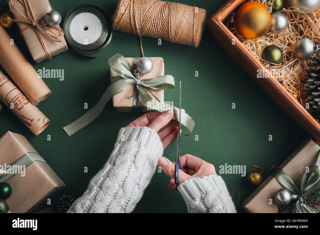 Hobby creativo. Le mani della donna avvolgono le feste di natale regalo fatto a mano in carta artigianale con nastro di spago. Fare arco a scatola regalo di Natale, decorato su oliv Foto Stock