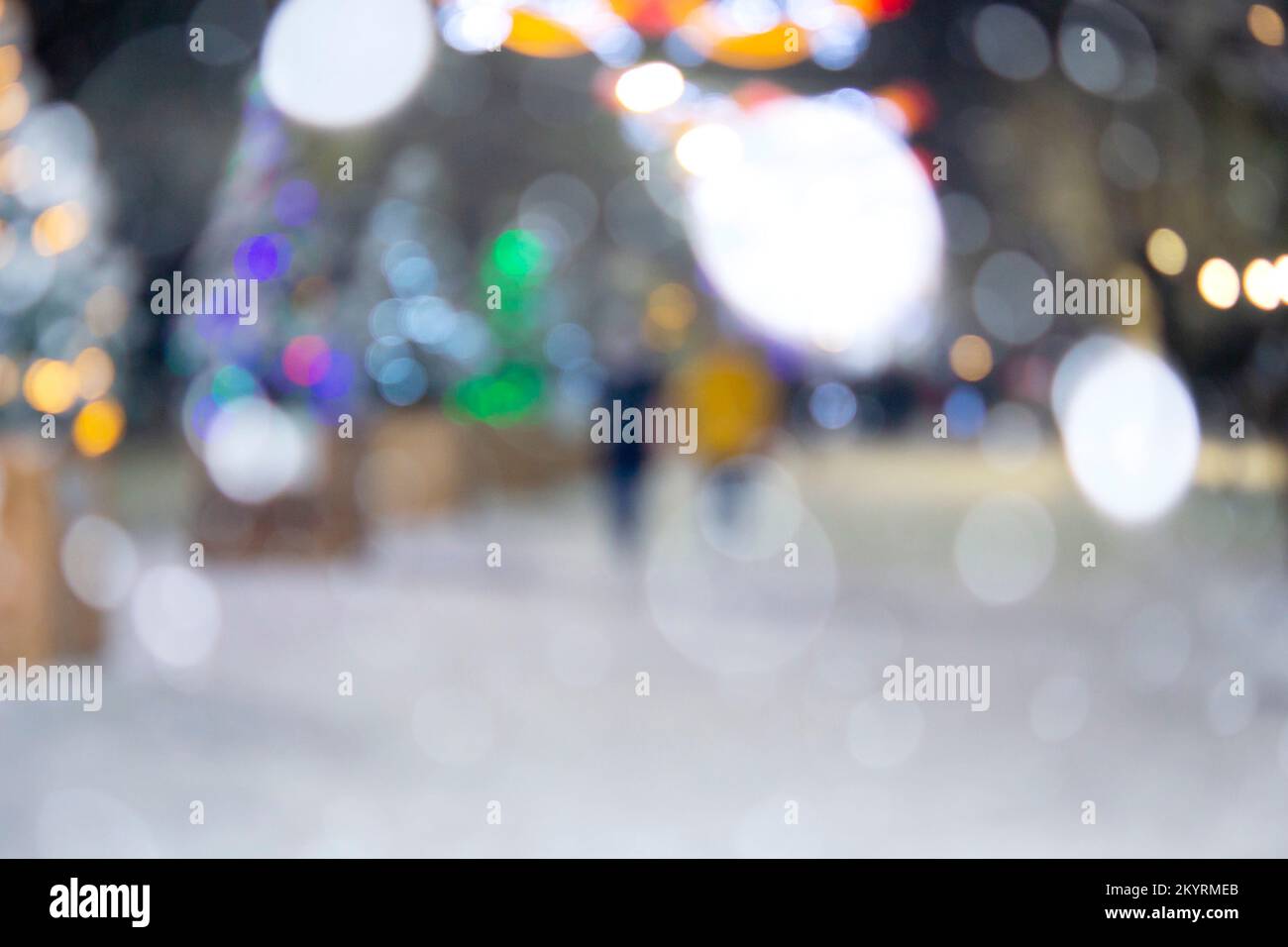 Sfondo sfocato. Strada cittadina durante le nevicate nella notte d'inverno. Molti alberi di Natale decorati, illuminazione, decorazione sulla strada. Festa di Natale di Capodanno. Lanterne ghirlande sugli alberi Foto Stock