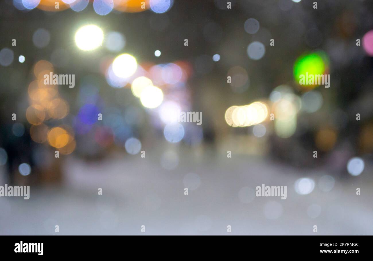 Sfondo sfocato astratto. Persone che camminano per strada di alberi di Natale decorati con illuminazione luminosa, luci incandescenti e ghirlande in città durante le pesanti nevicate nella notte d'inverno Foto Stock