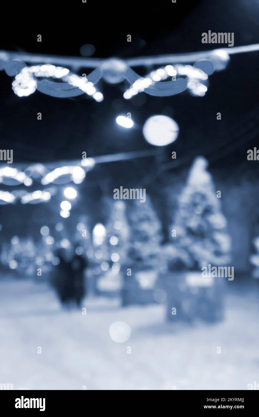 Sfondo sfocato astratto. Persone che camminano per strada di alberi di Natale decorati illuminazione luminosa decorata, luci e ghirlande in città durante la forte nevicata nella notte d'inverno colore blu Foto Stock