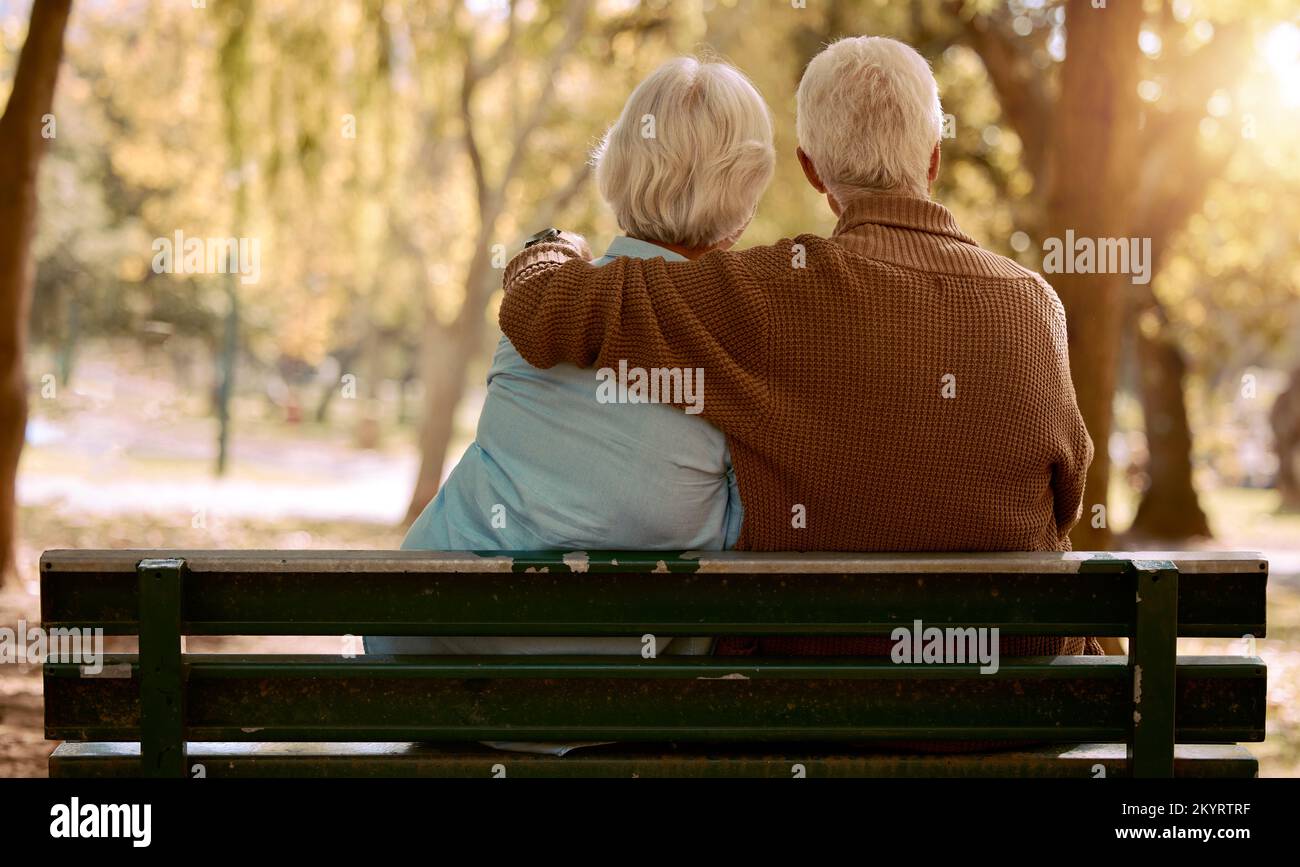 Amore, abbraccio e coppia anziana in un parco su una panchina per una tranquilla, pacifica o romantica data di matrimonio estivo anniversario. Natura, romanticismo o vista posteriore del vecchio Foto Stock