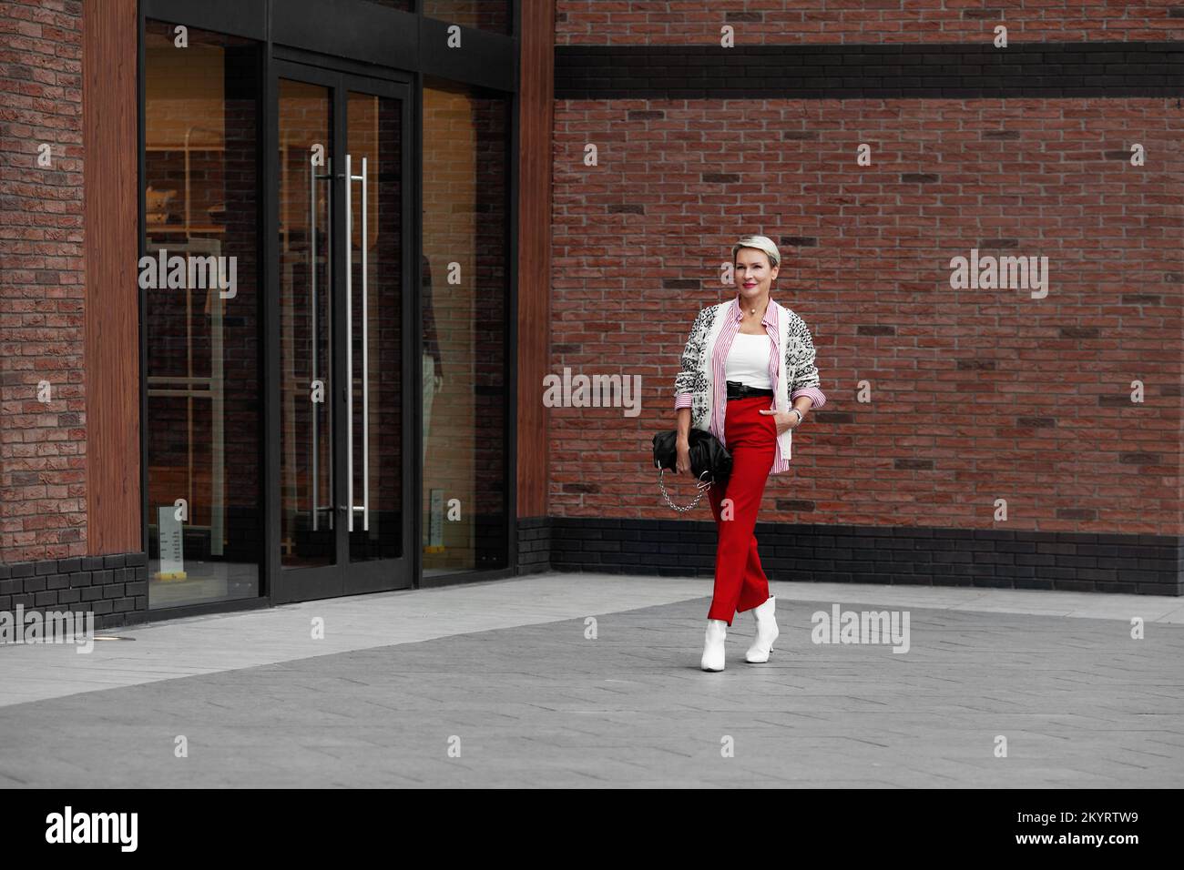 Autunno o primavera stile di strada vestiti tendenza. Abito luminoso casual per donna d'affari che cammina con fiducia lungo la strada. Modello che indossa maglione, camicia Foto Stock