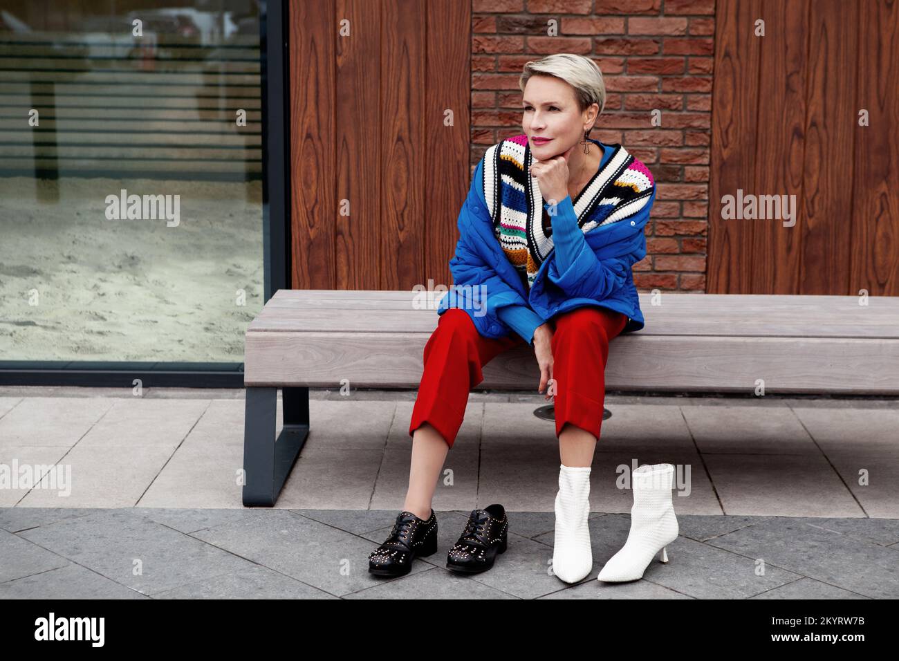 Stile Street. Adulto, donna bella seduta e pensare, scegliendo quali scarpe indossare, stivali bianchi o neri Foto Stock