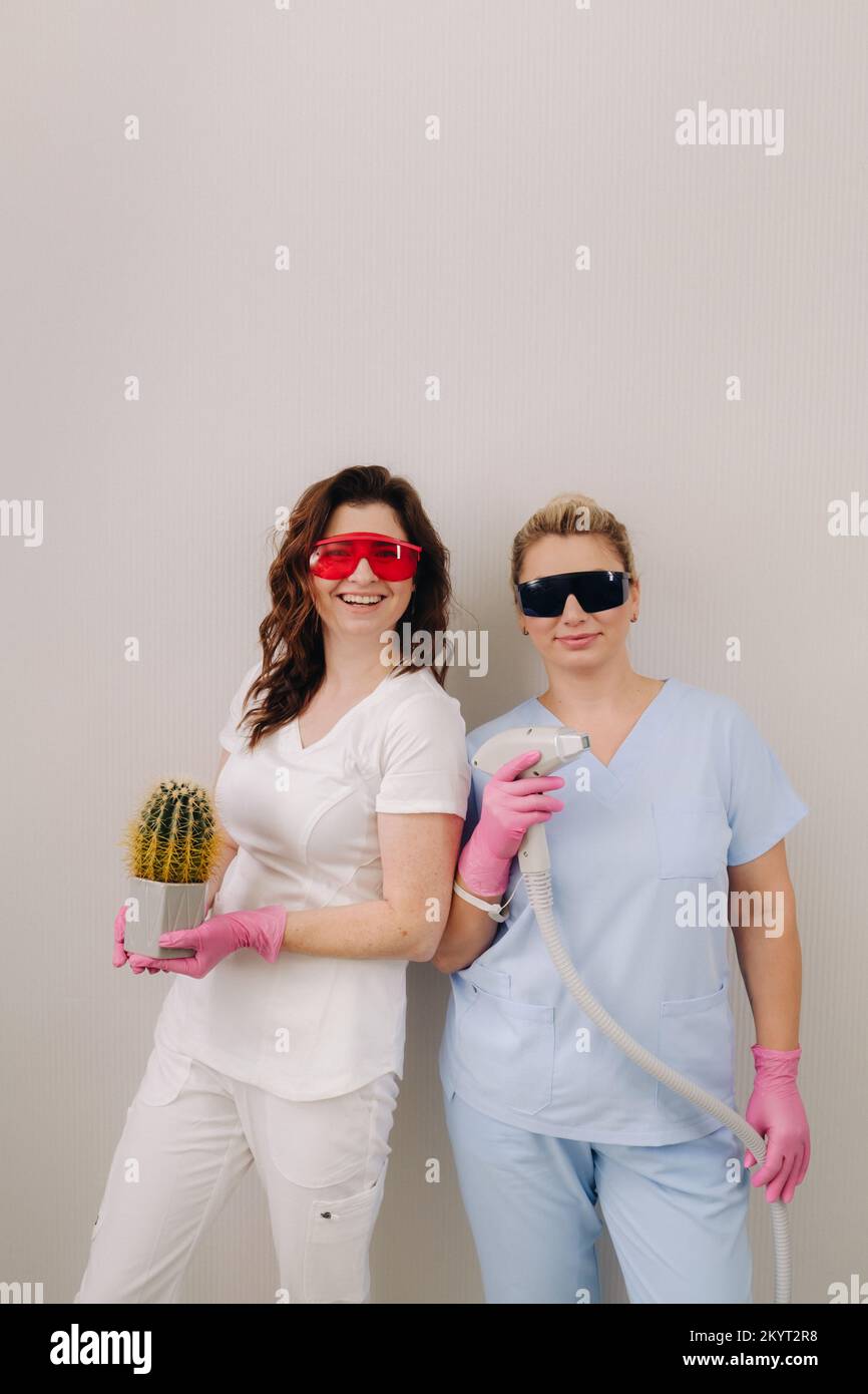 Due cosmetologi in occhiali protettivi stanno tenendo un dispositivo di depilazione laser e un cactus nelle loro mani Foto Stock