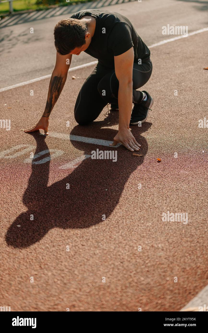 Un uomo muscoloso si sta preparando per uno sprint di 100 metri. È sulla linea di partenza in attesa di un cartello Foto Stock