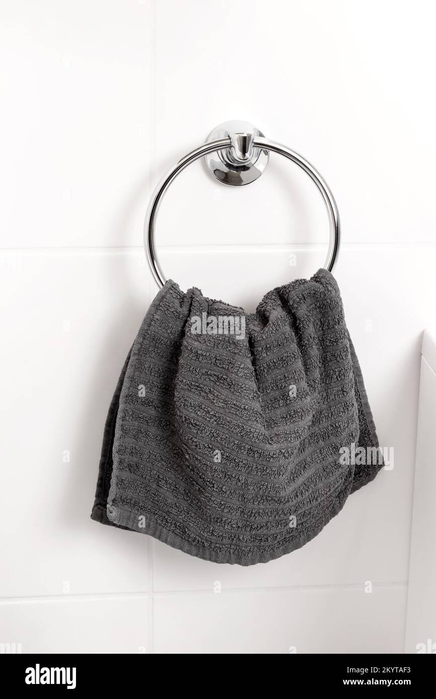 Asciugamano grigio appeso su un supporto ad anello cromato su una parete piastrellata bianca in un bagno moderno Foto Stock