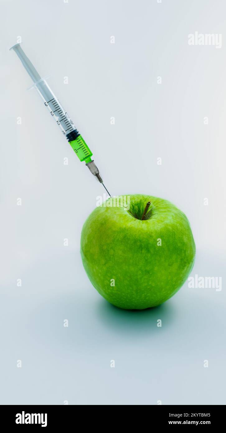 mela verde con una siringa che si attacca al suo interno iniettando liquido verde Foto Stock