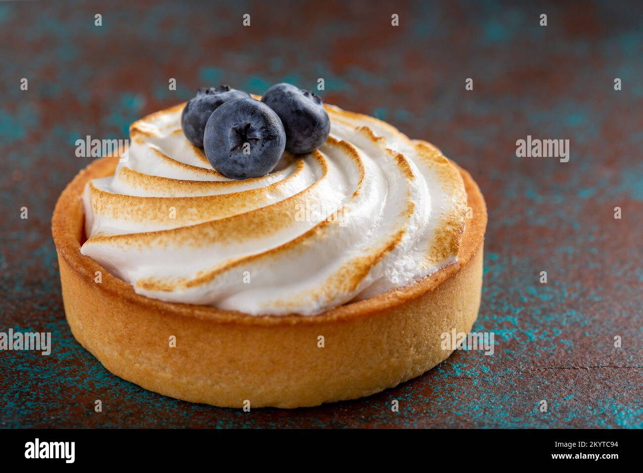 Deliziosa torta di cagliata al limone ricoperta di meringa e decorata con mirtilli, fondo scuro Foto Stock