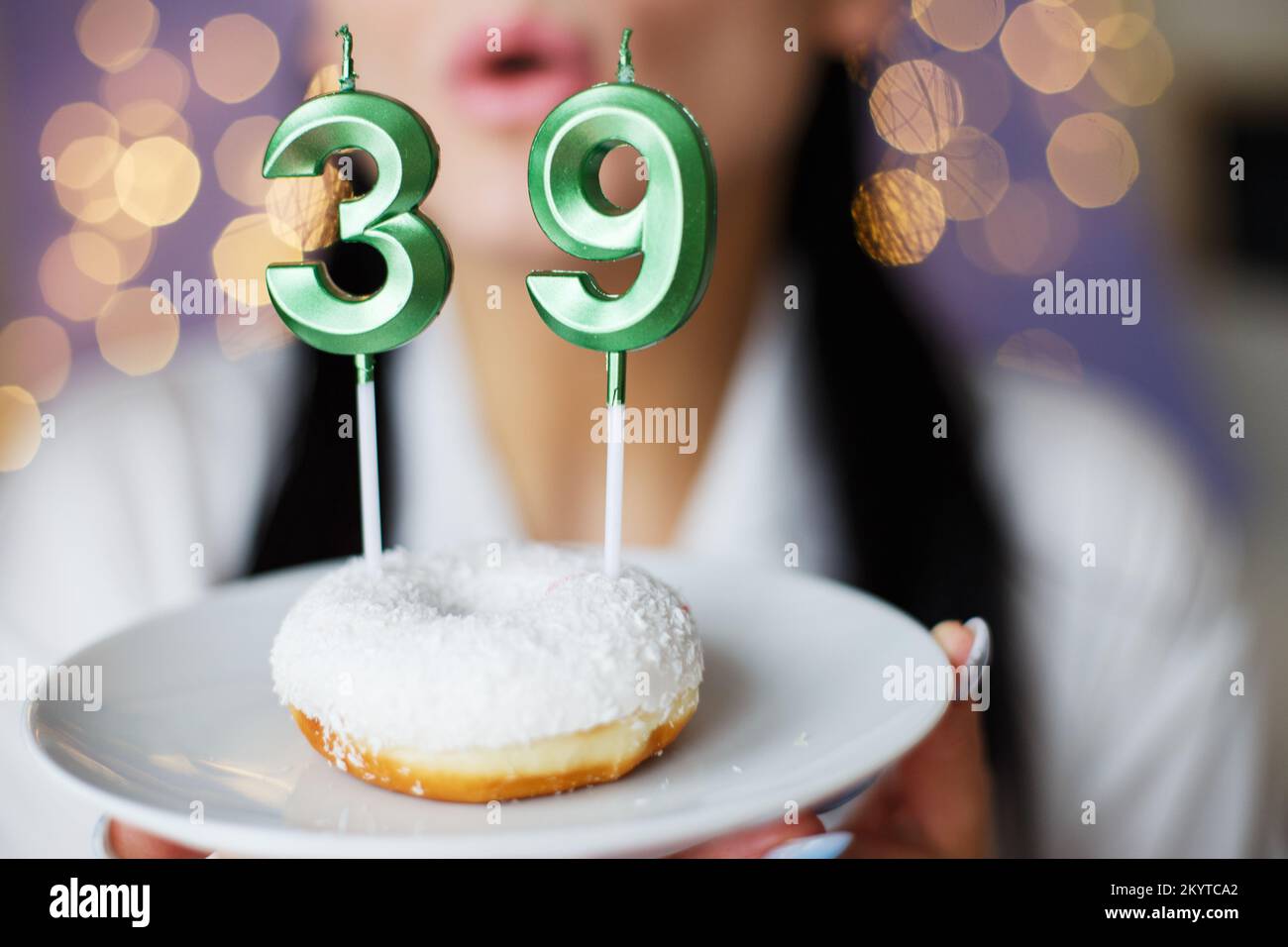 donna che tiene una torta con il numero 39 candele su sfondo bokeh sfocato festivo. Foto Stock