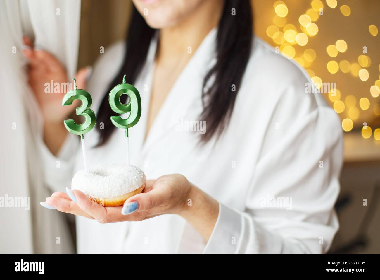 donna che tiene una torta con il numero 39 candele su sfondo bokeh sfocato festivo. Foto Stock