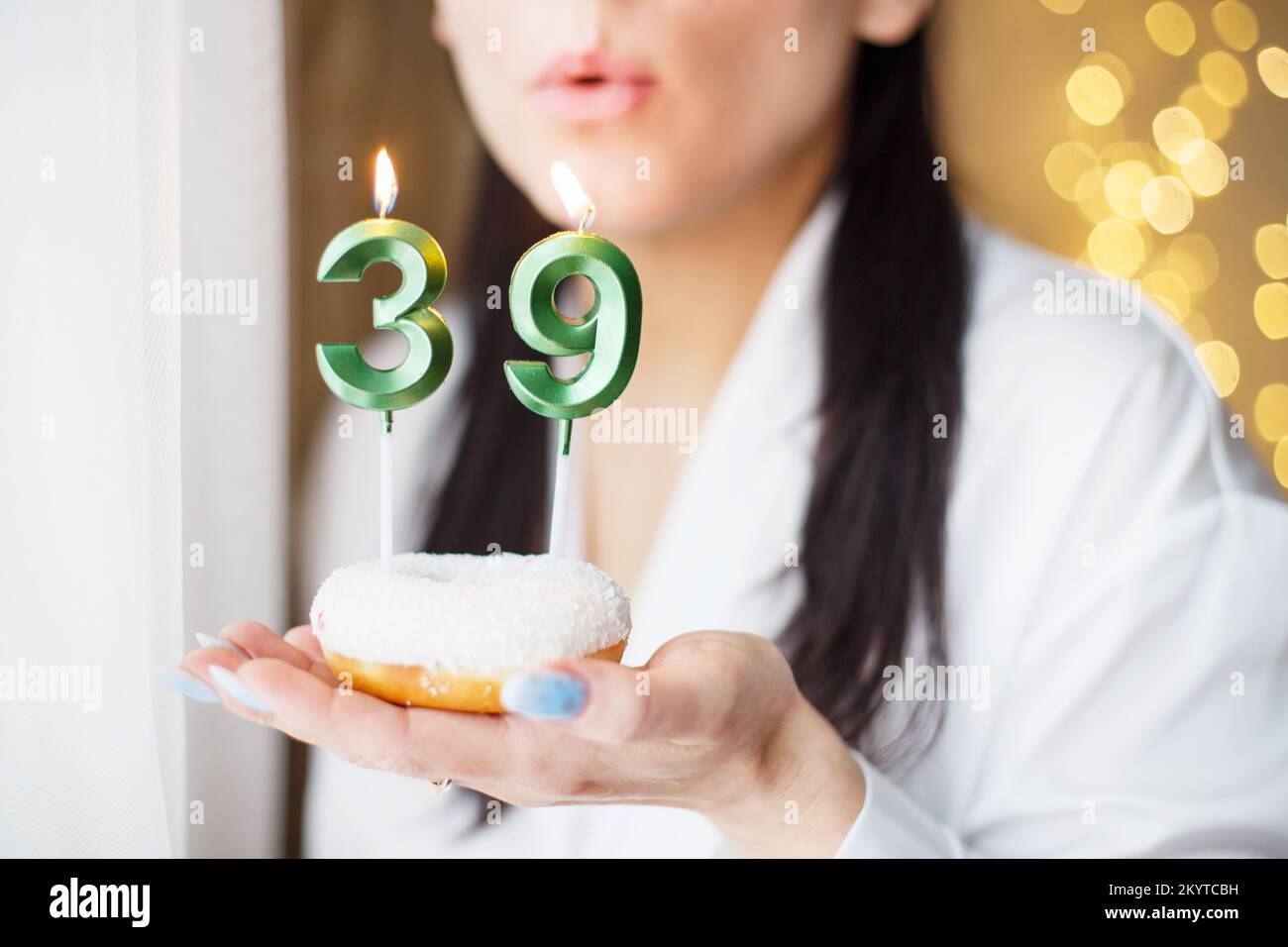 donna che tiene una torta con il numero 39 candele su sfondo bokeh sfocato festivo. Foto Stock