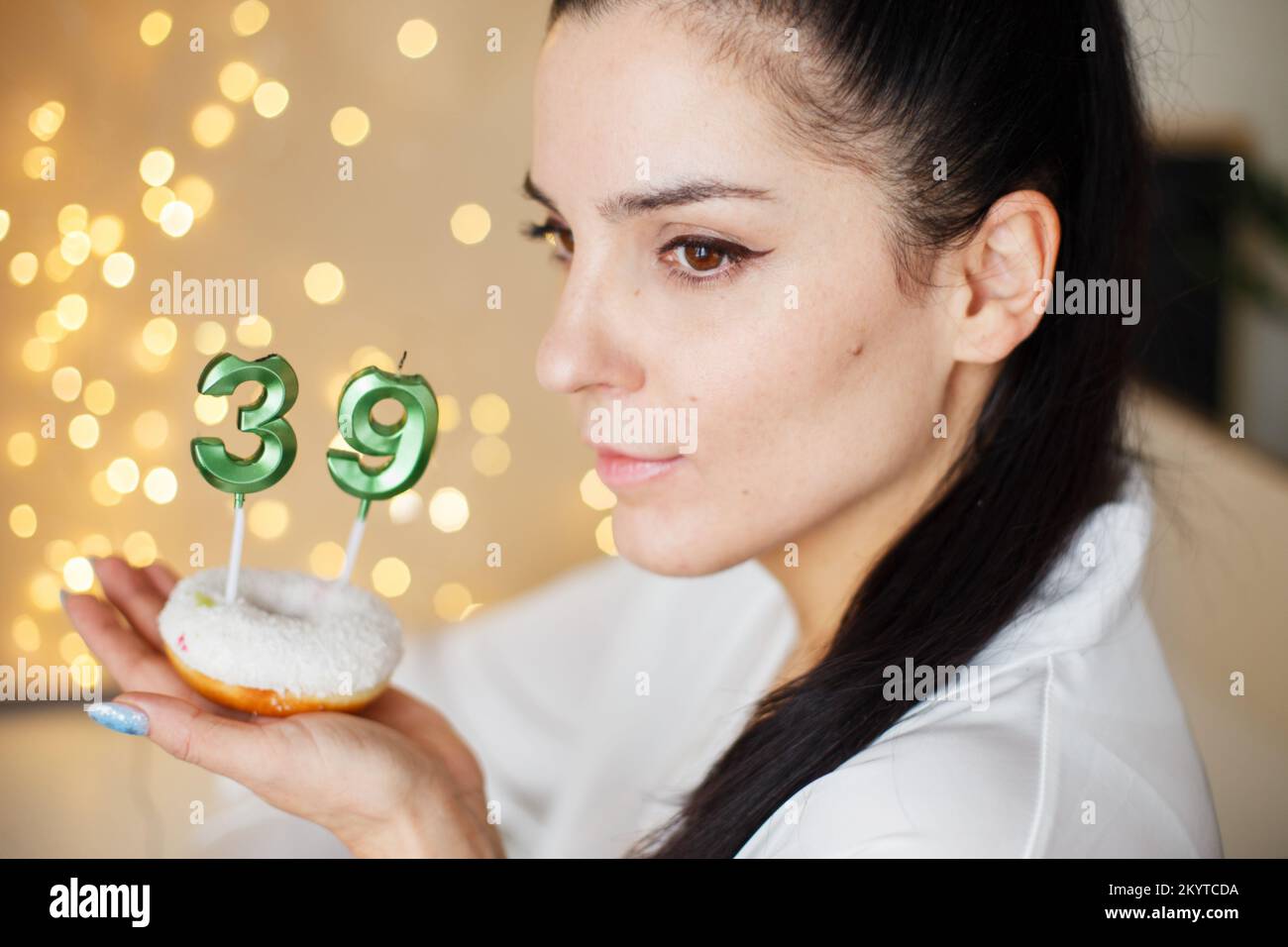 donna che tiene una torta con il numero 39 candele su sfondo bokeh sfocato festivo. Foto Stock