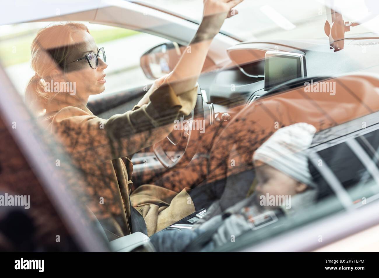 Madre che si concentra sulla guida di famiglia auto in esecuzione errands, mentre il suo bambino dorme in seggiolino auto per bambini dal suo sito Foto Stock