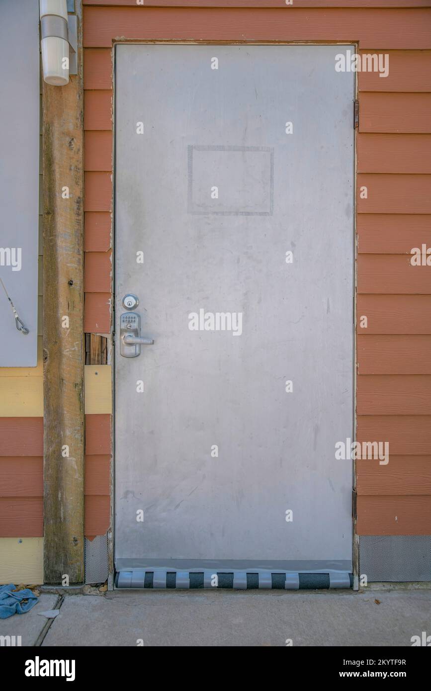 Porta con serratura a tastiera in acciaio inossidabile di un edificio con lap in vinile marrone sul lago Austin-Austin, Texas. Vecchia porta con un pilastro a sinistra con parete lam Foto Stock