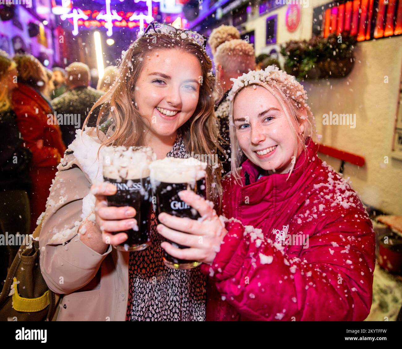 Bronagh McCarron (a sinistra) e Shannon Gillespie sulle strade acciottolate del Commercial Court fuori del bar Duke of York a Belfast, mentre Guinness ha dato vita al suo iconico annuncio natalizio con una macchina da neve mentre gli ospiti sono stati accolti da una pinta per iniziare le feste. Foto Stock