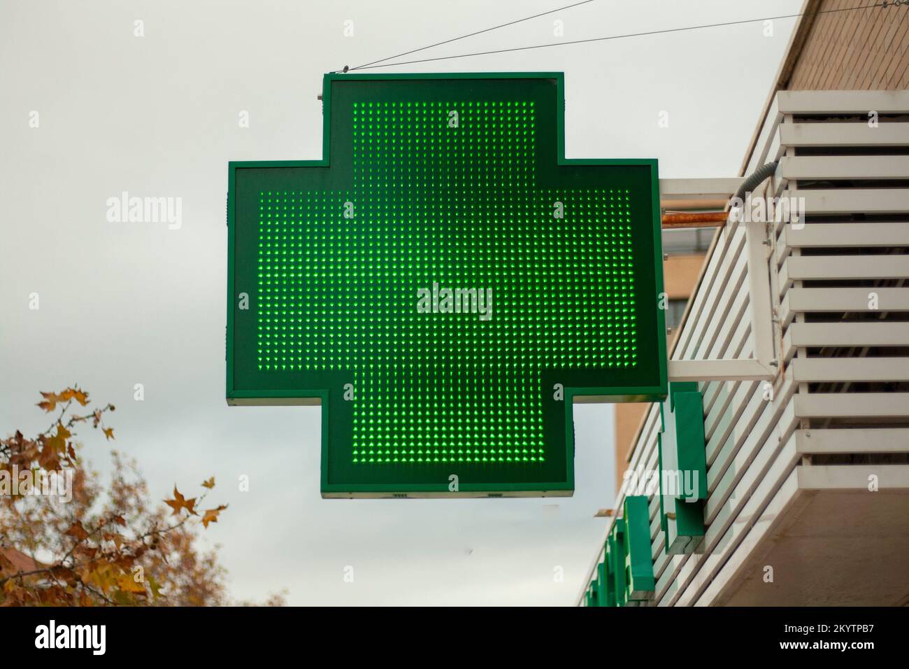 Croce verde luminosa che indica che una farmacia rimane aperta nella città di Madrid Foto Stock