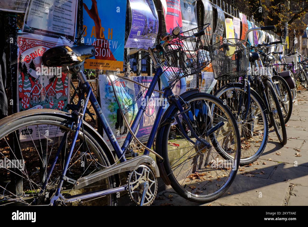 Una collezione di vecchie biciclette sul marciapiede incatenate a ringhiere coperte da poster a Cambridge, Regno Unito Foto Stock