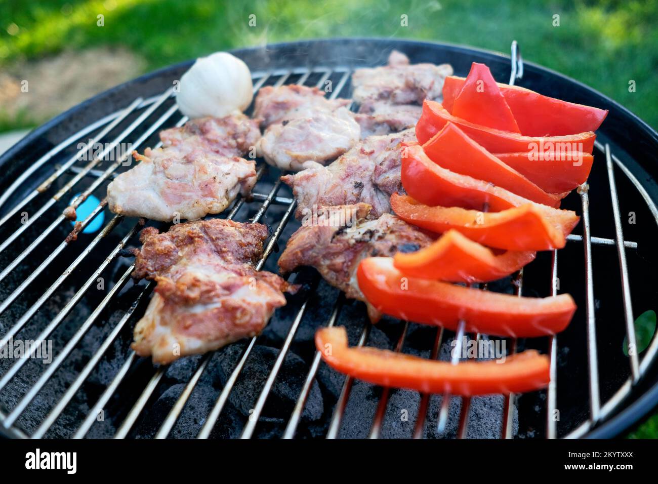 Bistecche di maiale e peperoni rossi che cucinano all'aperto su un barbecue a carbone Foto Stock