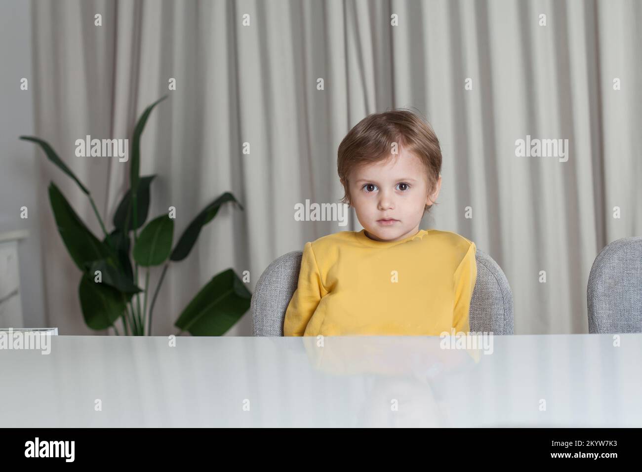 Ragazzo felice con capelli castani in maglione giallo seduto al tavolo Foto Stock