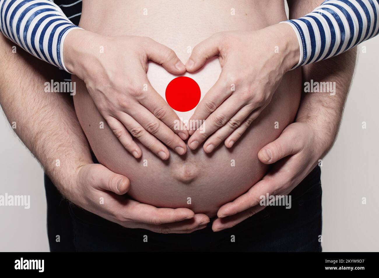 Concetto di famiglia Giapponese. Uomo che abbraccia il ventre e il cuore di donna incinta con bandiera del Giappone colori primo piano Foto Stock
