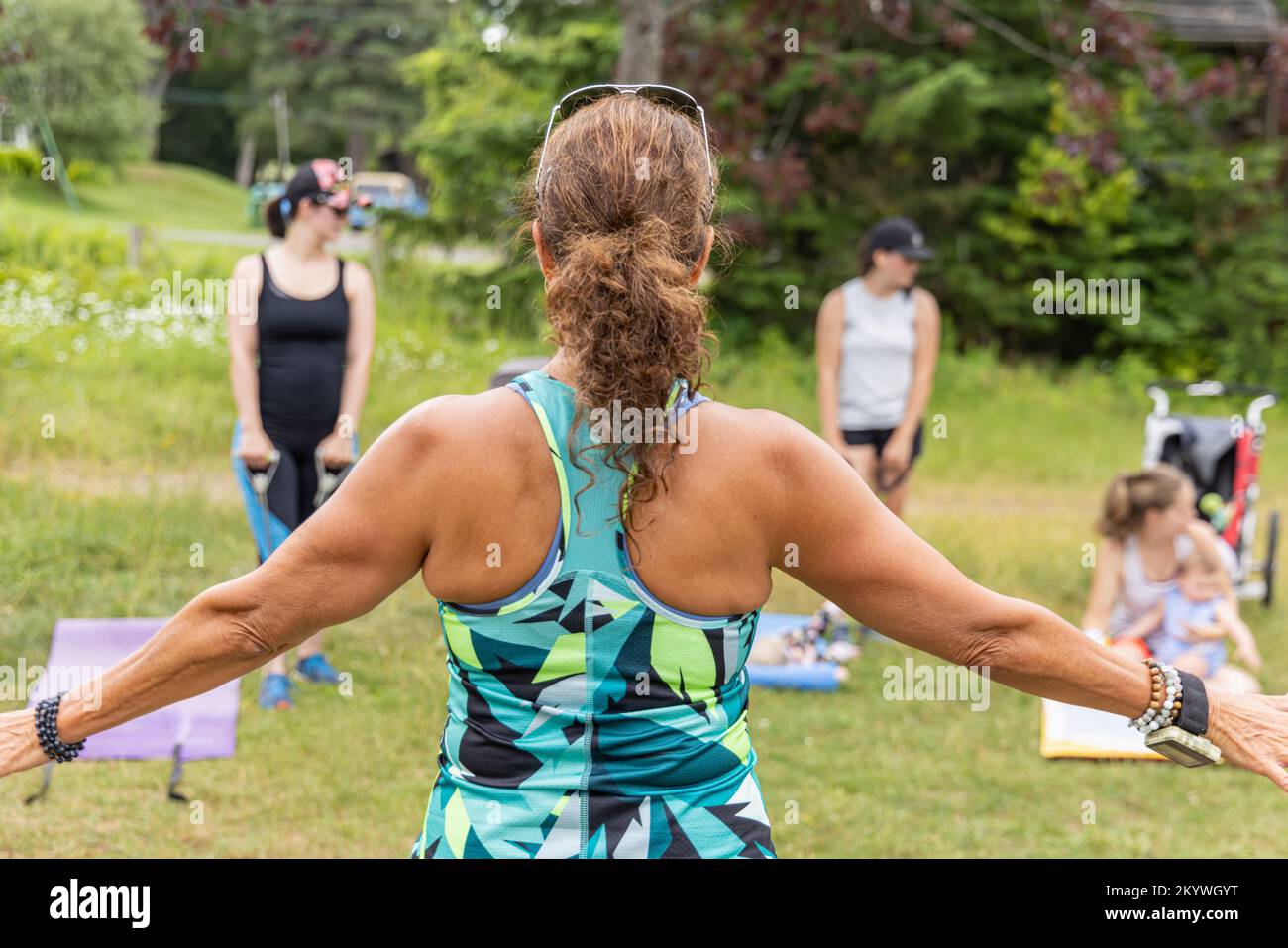 Foto sul retro scattata da un istruttore che dà istruzioni all'esterno su un campo d'erba alle madri con i loro figli che lavorano sulla loro salute Foto Stock