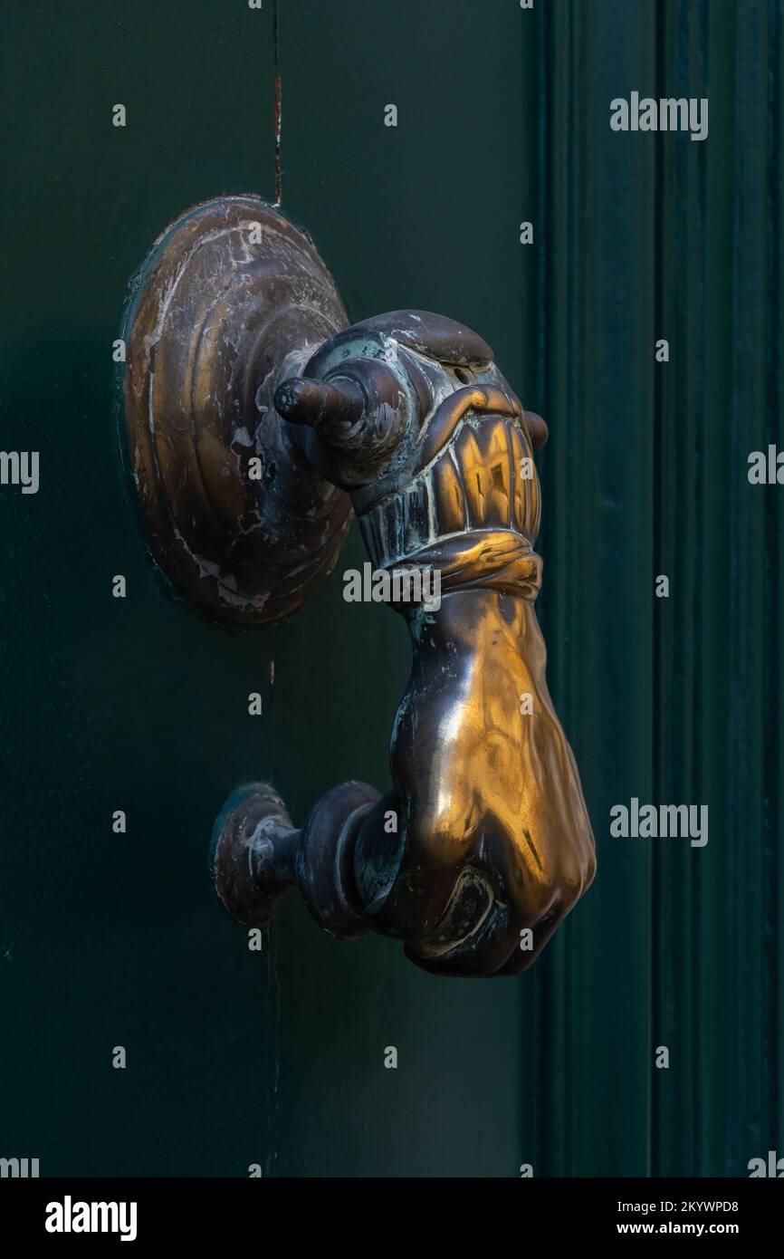 Vista closeup di elegante porta battente in ottone vintage a forma di mano che tiene la palla isolato su porta di legno verde scuro, Montpellier, Francia Foto Stock