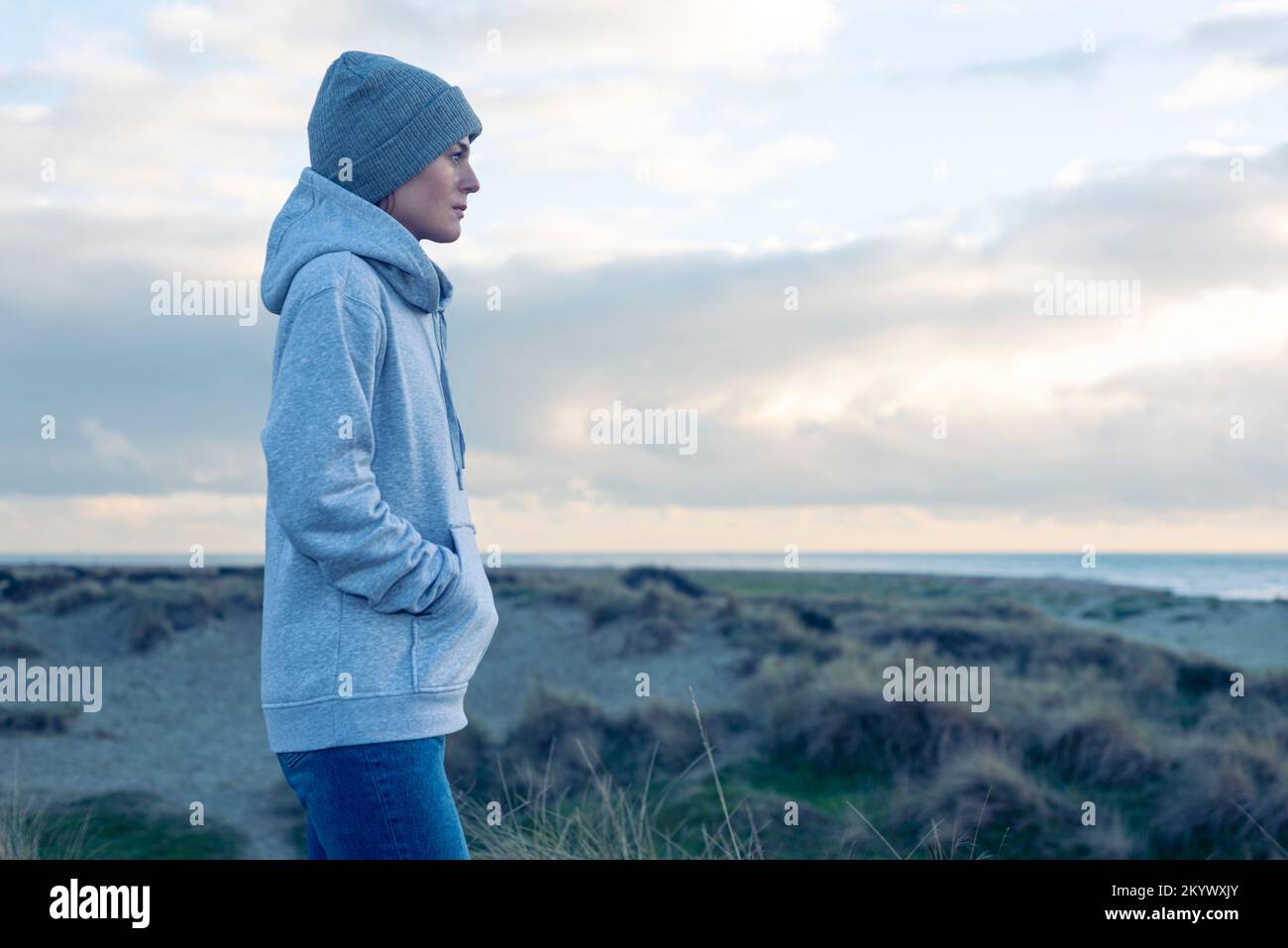 Donna fuori per una passeggiata sul mare, da sola. indossa un cappello e una felpa con cappuccio calda. Foto Stock