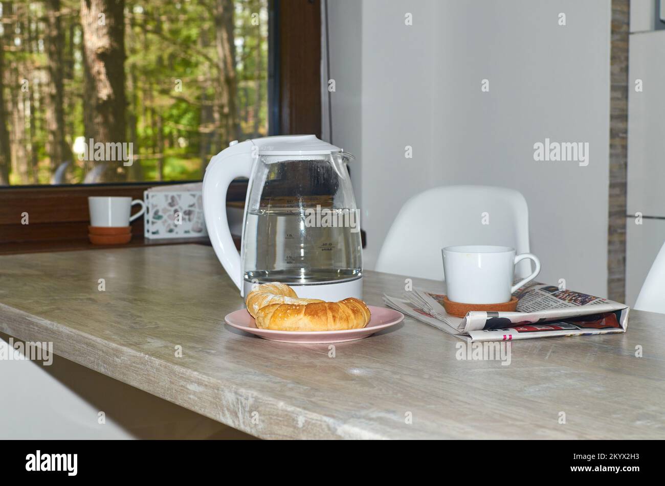 Croissant e una tazza di caffè sono serviti su una colazione al tavolo con un albero verde visto da una finestra dietro Foto Stock