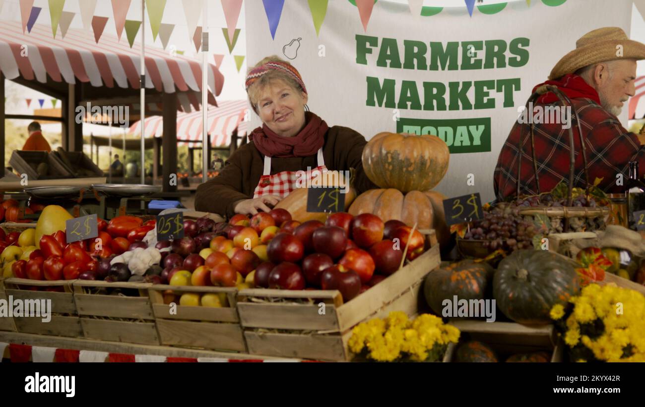 Donna contadina si alza presso la stalla con frutta e verdura fresca e colorata, guarda la macchina fotografica. Festa del mercato degli agricoltori. Cibo vegetariano, biologico e sano. Agricoltura. Foto Stock