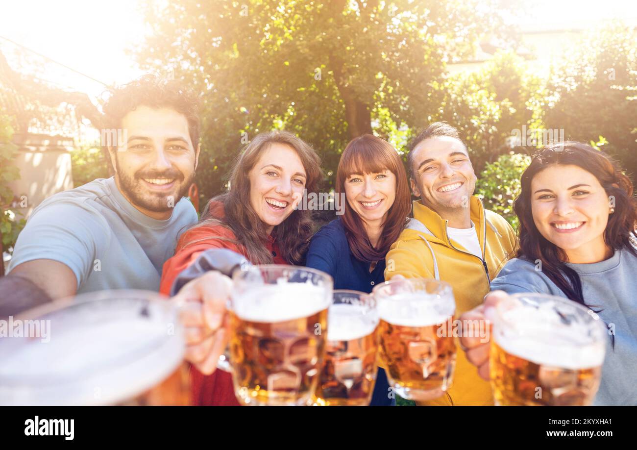 Gruppo di amici che brindano bicchieri da birra all'aperto nella fattoria - Gruppo di studenti che si divertono alla festa di compleanno nel ristorante giardino Foto Stock