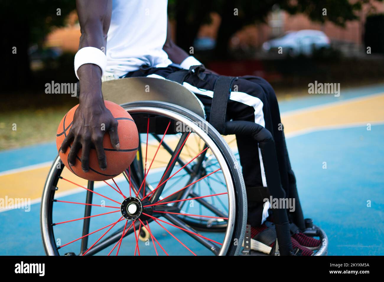 Un atleta campione con disabilità che gioca a basket all'aperto. Ritratto dell'uomo afroamericano con palla guardando la fotocamera e sorridendo. Concetto di Foto Stock