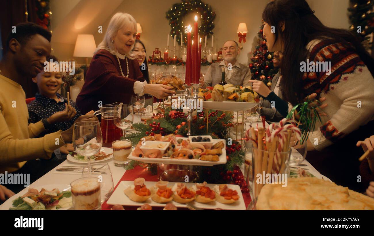 Buona famiglia seduto al tavolo e festeggia Natale o Capodanno a casa. Nonna ha impostato il tavolo con piatto tradizionale tacchino. Calda atmosfera della cena di Natale in famiglia. Vigilia di Natale. Foto Stock