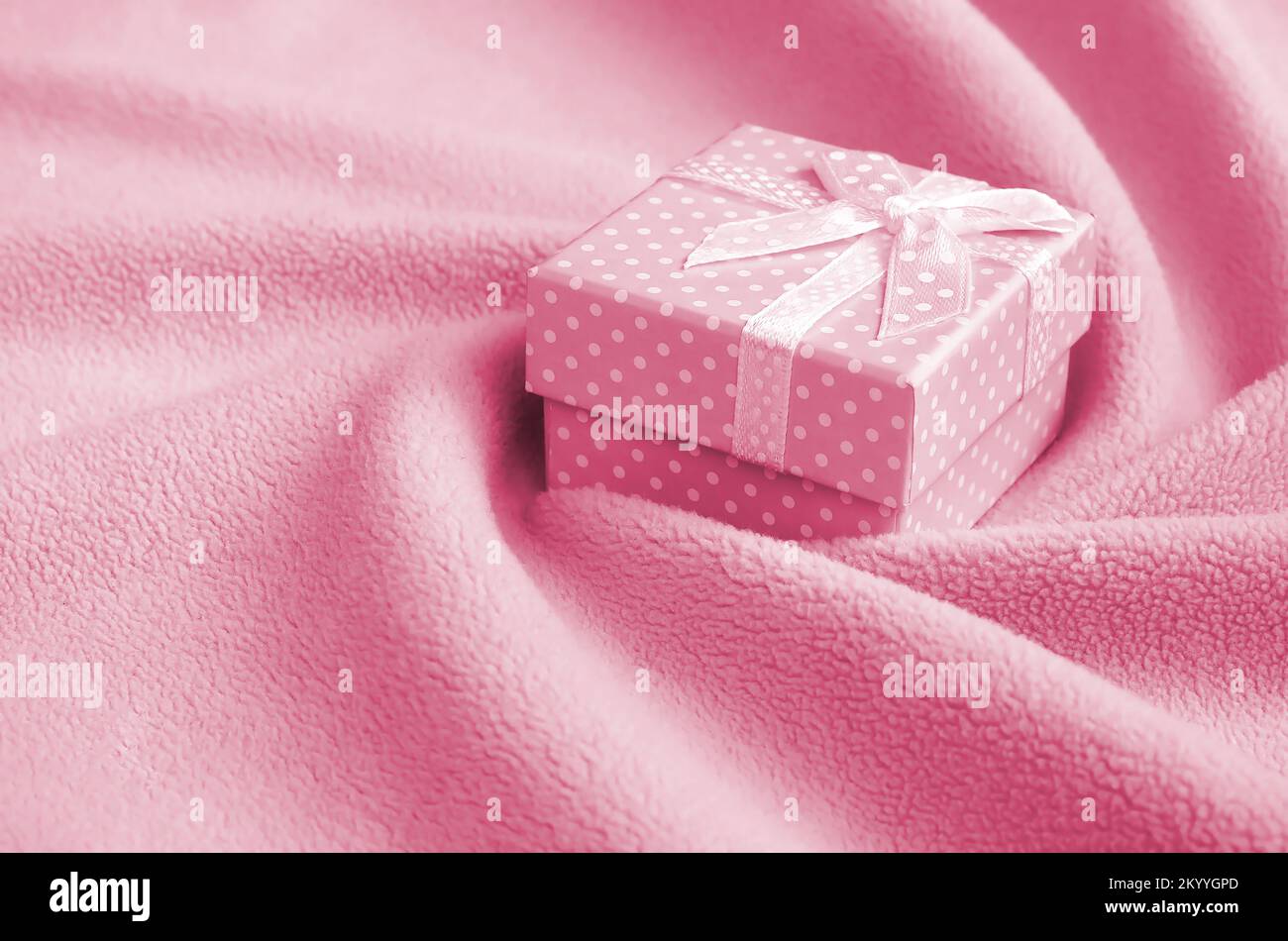 Una piccola scatola regalo con un piccolo arco si trova su una coperta di  tessuto di pile con un sacco di pieghe in rilievo. Imballaggio per un regalo  alla vostra ragazza graziosa.