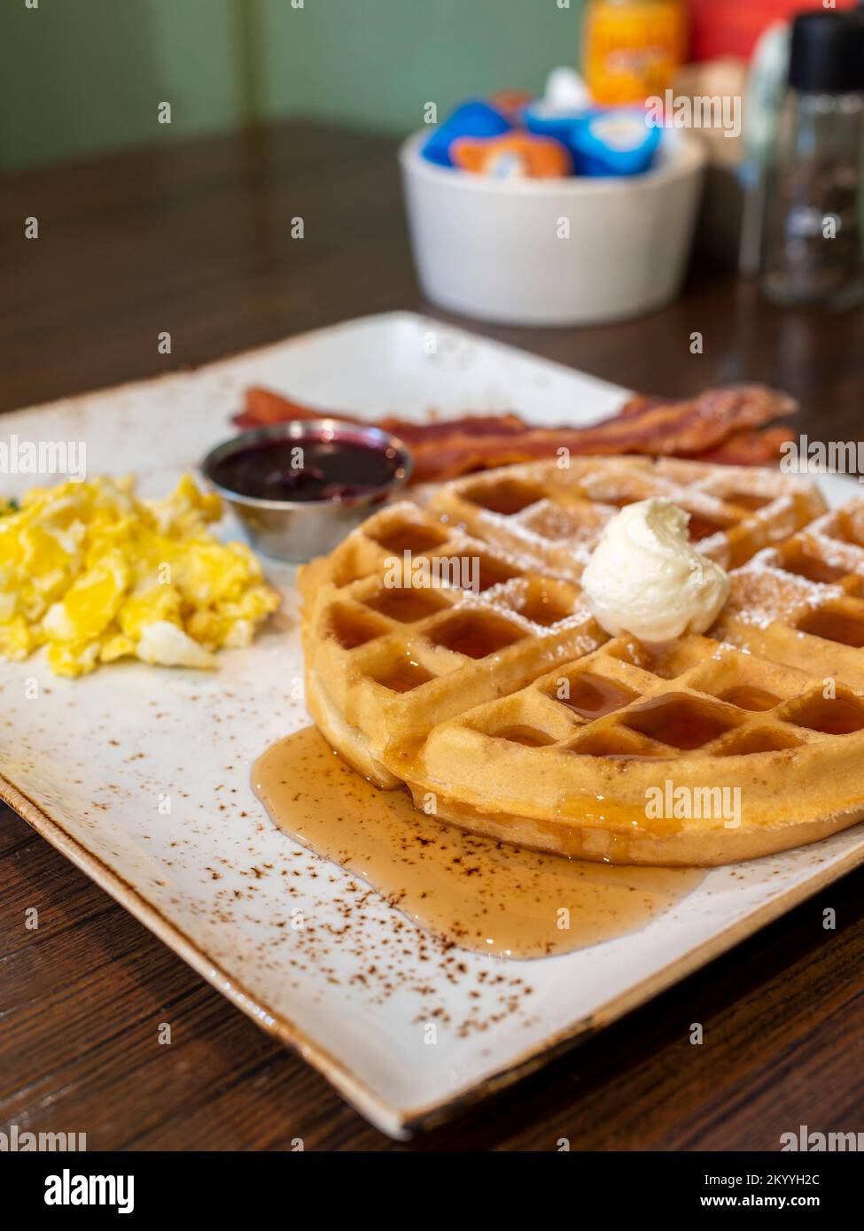 Colazione all'americana con waffle belgi, uova strapazzate e pancetta su un piatto quadrato al ristorante First Watch di Montgomery, Alabama, USA. Foto Stock