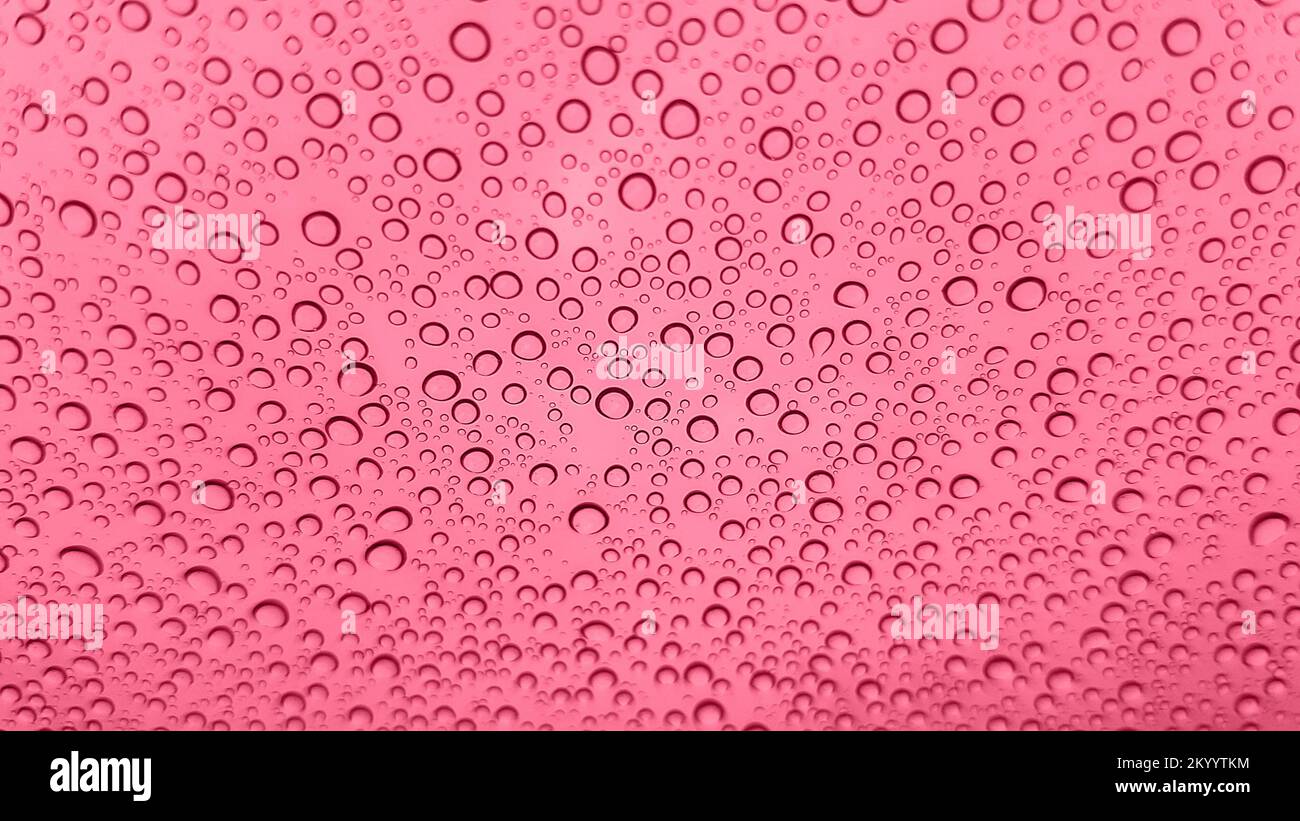 Colore dell'anno 2023 Viva Magenta. L'immagine astratta delle gocce di pioggia sul vetro è tonata nel colore pantone di viva magenta. Nuovo colore moda. Vista dall'alto. Abstra Foto Stock