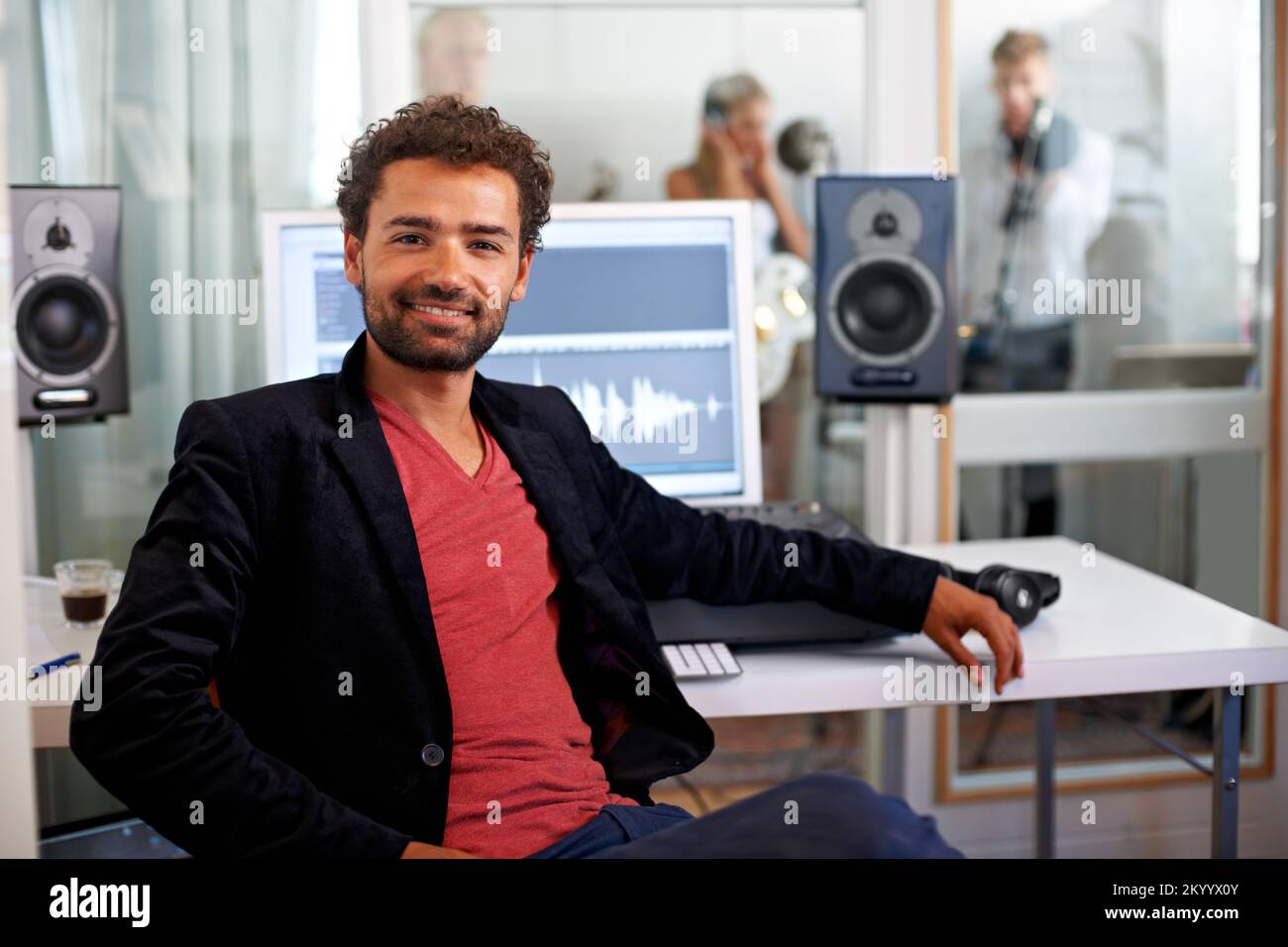 Pronti a realizzare i vostri sogni. Un bel giovane ingegnere audio seduto nel suo studio con una band sullo sfondo. Foto Stock