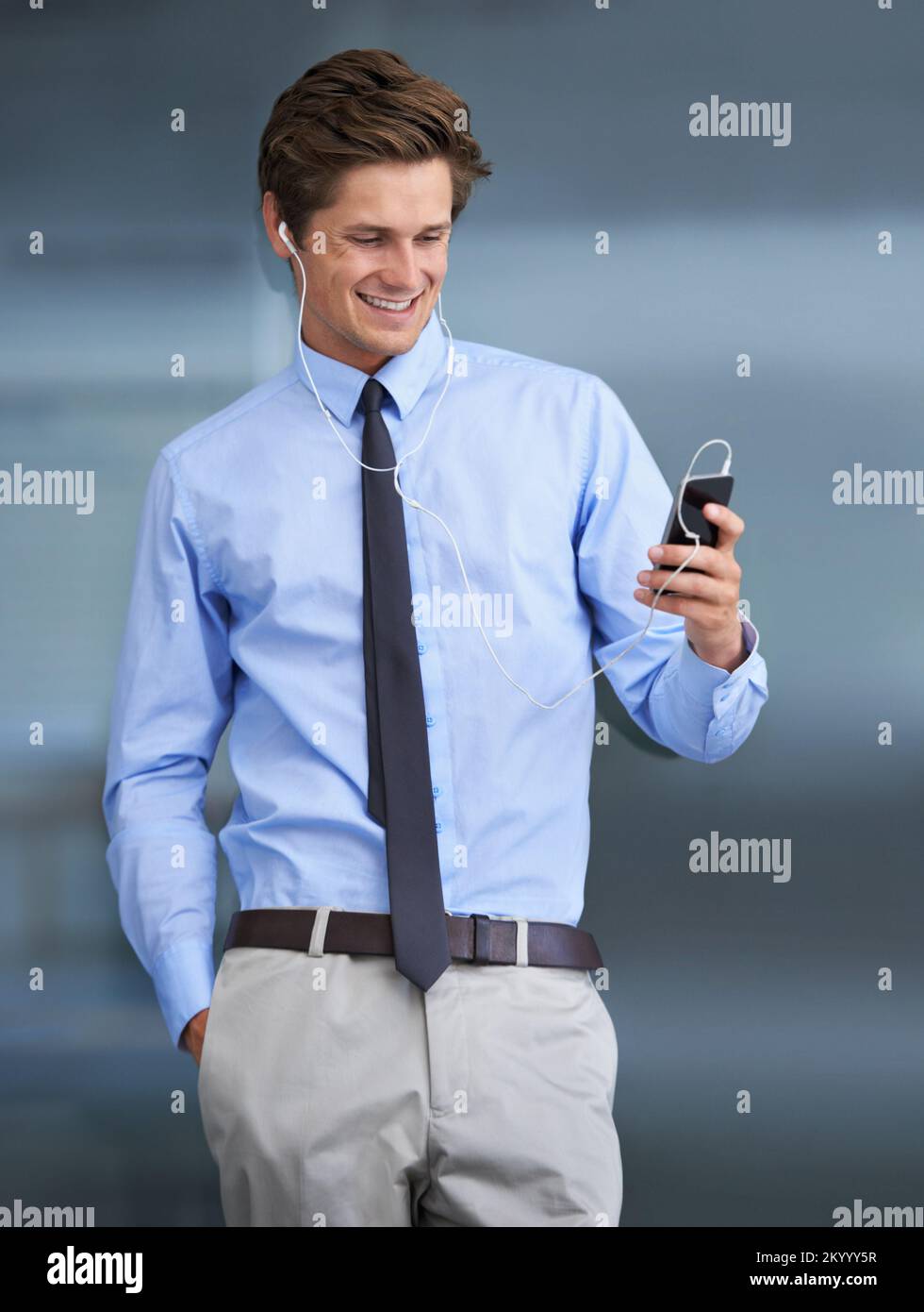 Selezionando alcuni dei suoi preferiti. Un bel giovane uomo d'affari che usa il suo smartphone come lettore mp3. Foto Stock