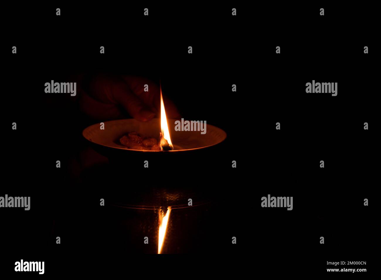 Una corda in olio giace su un piatto e brucia nella mano della ragazza al buio, una candela fatta in casa sullo specchio Foto Stock