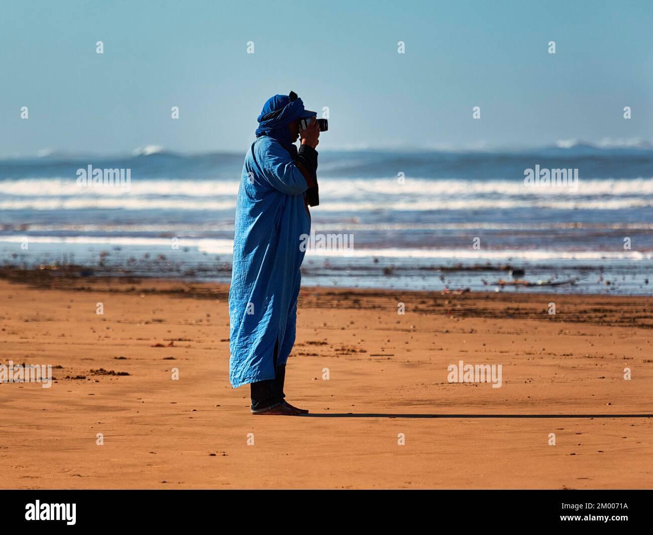 Fotografo, berbero in tipico abbigliamento blu fotografato sulla spiaggia, Plage Tagharte, Essaouira, Oceano Atlantico, Maro Foto Stock