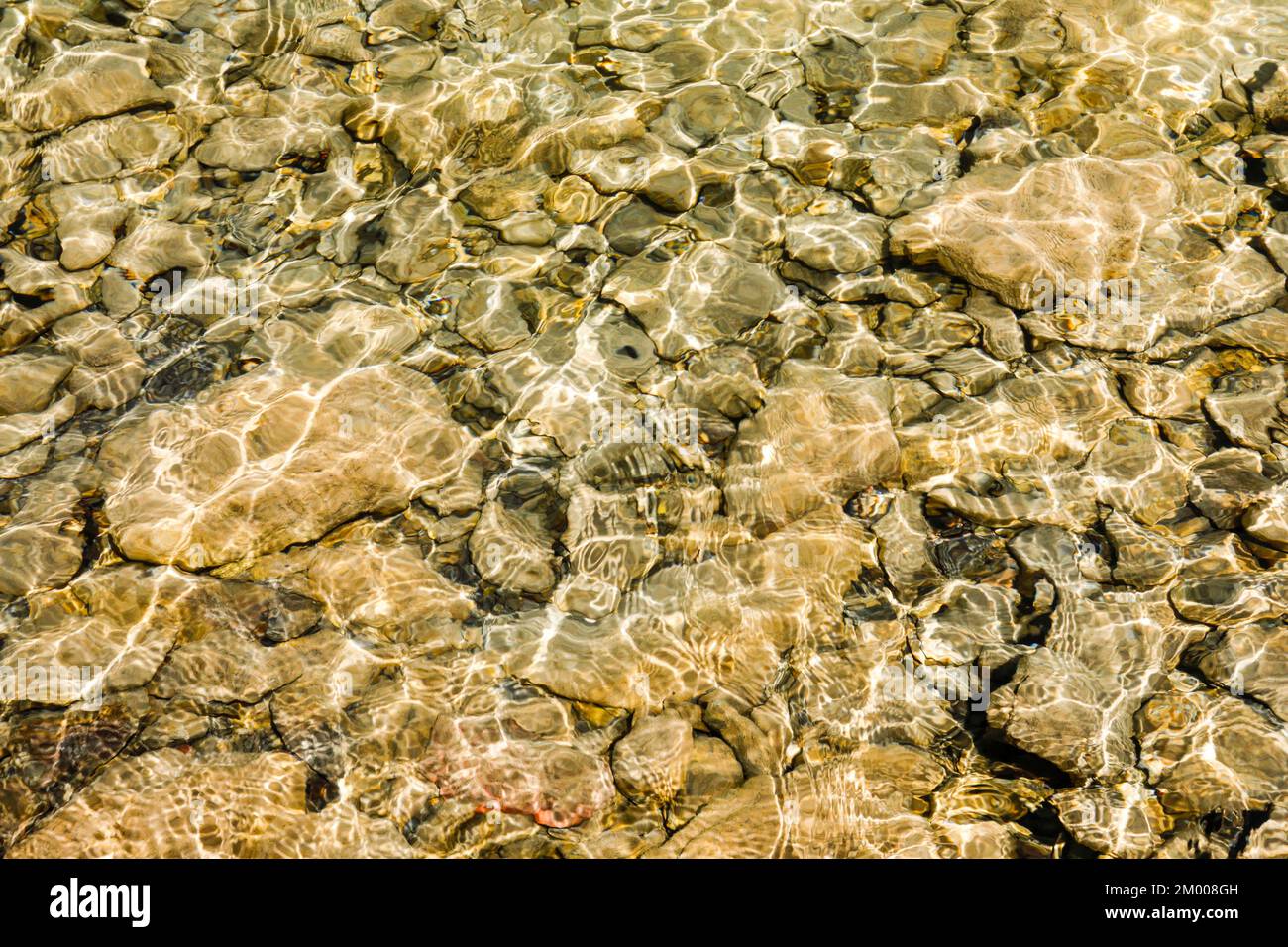 Il sole proietta un affascinante gioco di luci e ombre sulle acque cristalline e sulle pietre beige-marroni sulle rive del lago Walen, Canton St Gallen, Svizzera, E. Foto Stock