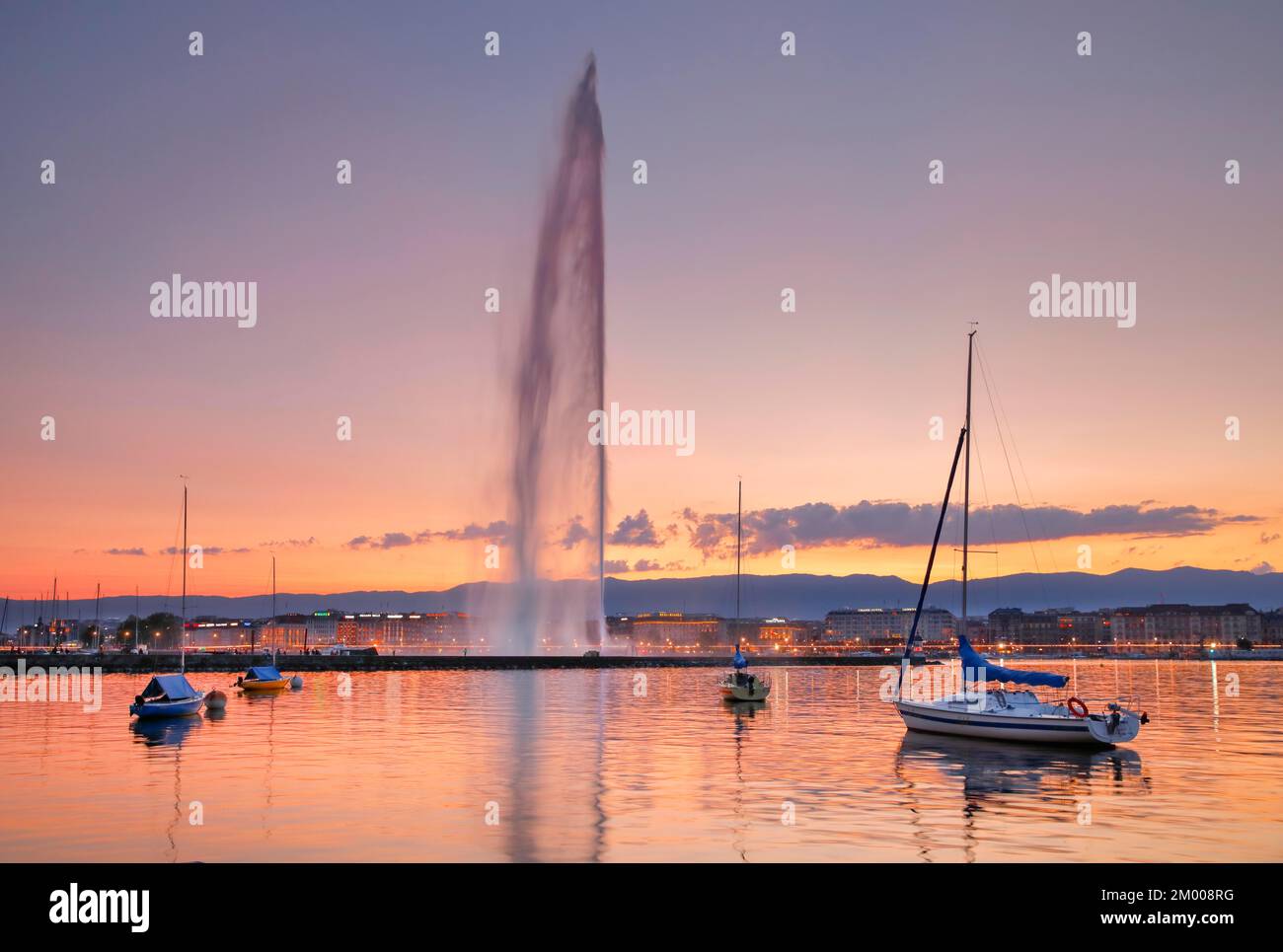Il Jet d'eau al crepuscolo è il punto di riferimento nel bacino del Lago di Ginevra, con barche a vela in primo piano e il lungolago illuminato di notte nel backgro Foto Stock