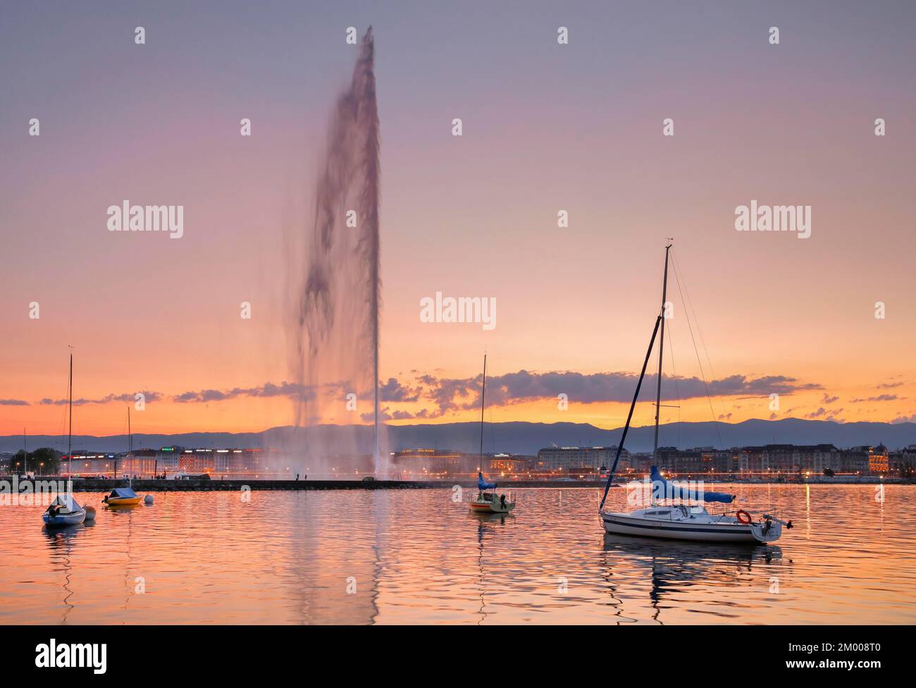 Il Jet d'eau al crepuscolo è il punto di riferimento nel bacino del Lago di Ginevra, con barche a vela in primo piano e il lungolago illuminato di notte nel backgro Foto Stock