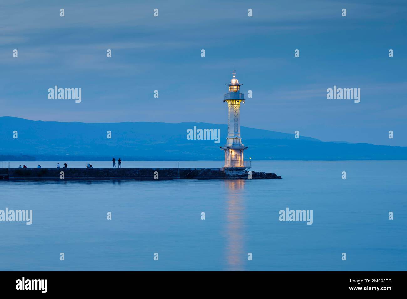 I turisti che si godono il crepuscolo vicino al faro vicino alla parete del porto presso il bacino del Lago di Ginevra, Canton Ginevra, Svizzera, Europa Foto Stock