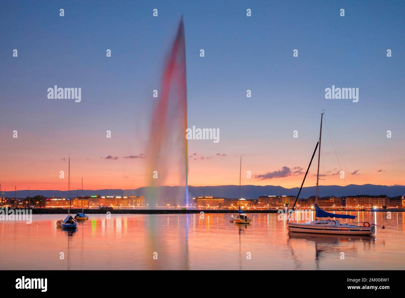 Il Jet d'eau al crepuscolo è il punto di riferimento nel bacino del porto di Ginevra, con barche a vela in primo piano e il lungolago illuminato di notte sul dorso Foto Stock