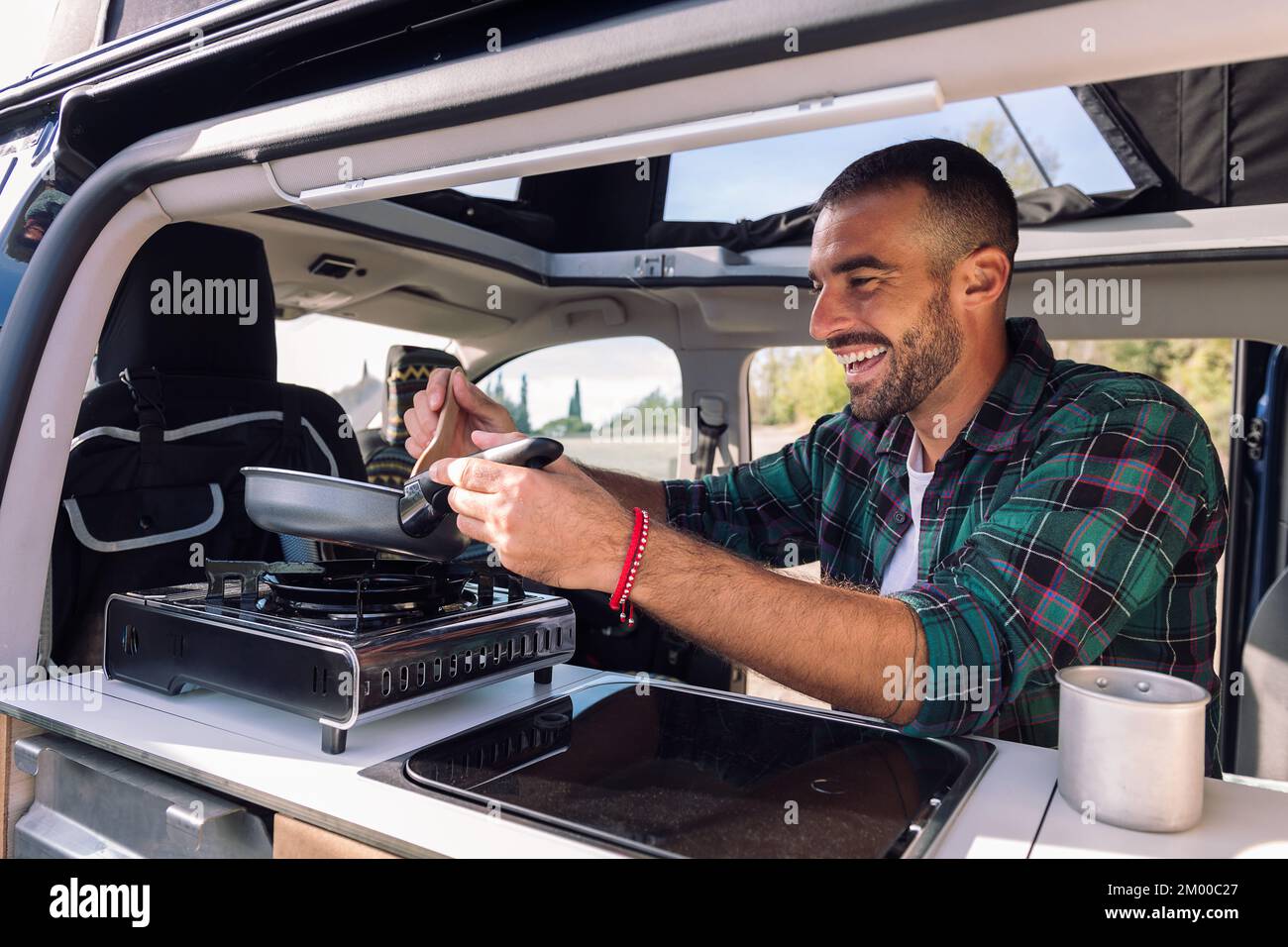 uomo che cucina con una padella nel suo camper Foto Stock